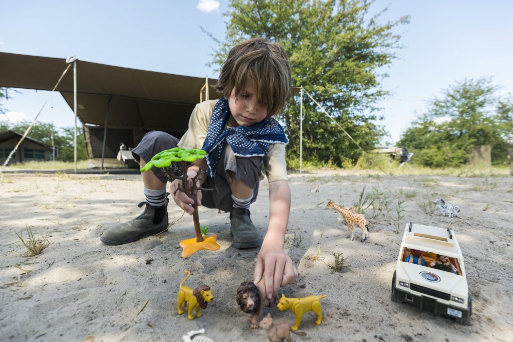 A boy setting up a safari scene with toy jeeps and wild animal toys and a tall tree